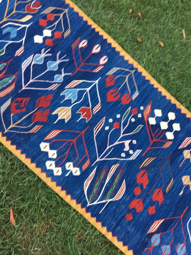 May include: A blue and yellow patterned rug with a floral design. The rug has a geometric pattern with red, white, and blue flowers.