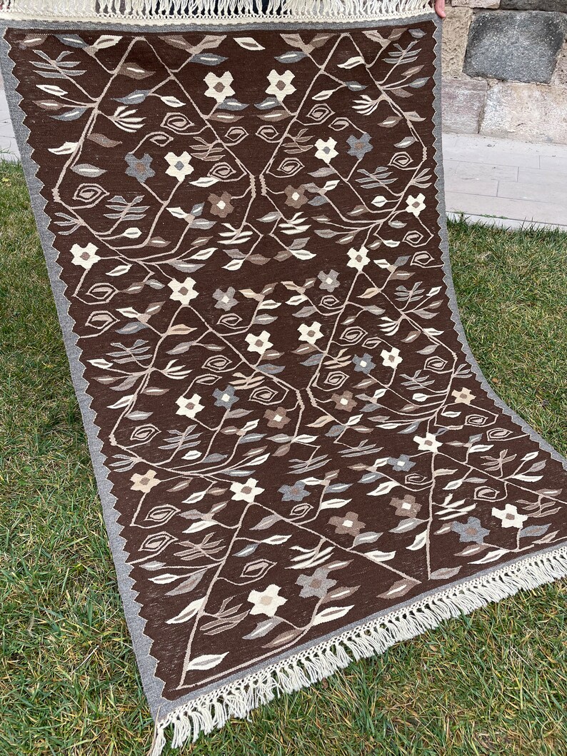 Puede incluir: Una alfombra marr&oacute;n y blanca con estampado y borde de flecos. La alfombra presenta un dise&ntilde;o floral con hojas y flores.