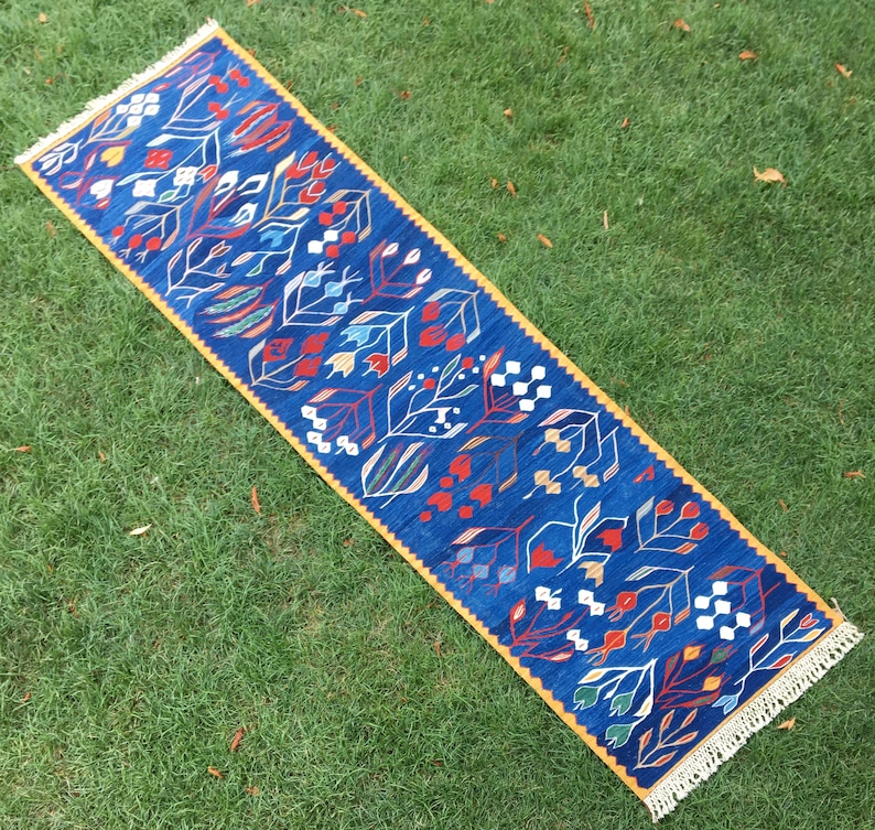 May include: A blue and yellow patterned runner rug with a fringe border. The rug features a floral design with red, white, and blue accents.