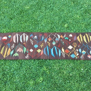 Puede incluir: Una alfombra larga y estrecha con fondo marr&oacute;n y un patr&oacute;n geom&eacute;trico colorido. El patr&oacute;n presenta flores y hojas estilizadas en tonos de rojo, azul, amarillo, verde y blanco.
