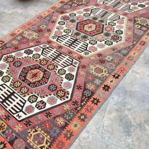 May include: A traditional Turkish rug with a geometric pattern in shades of red, orange, black, white, and blue. The rug has a central medallion and repeating motifs.