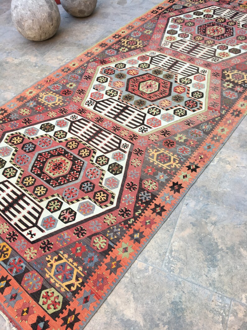 May include: A traditional Turkish rug with a geometric pattern in shades of red, orange, black, white, and blue. The rug has a central medallion and repeating motifs.