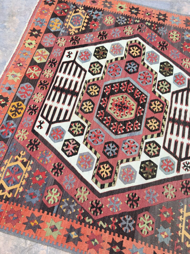 May include: A traditional Turkish rug with a geometric pattern in shades of red, blue, green, and white. The rug features a central medallion with a repeating pattern of hexagons and stars.