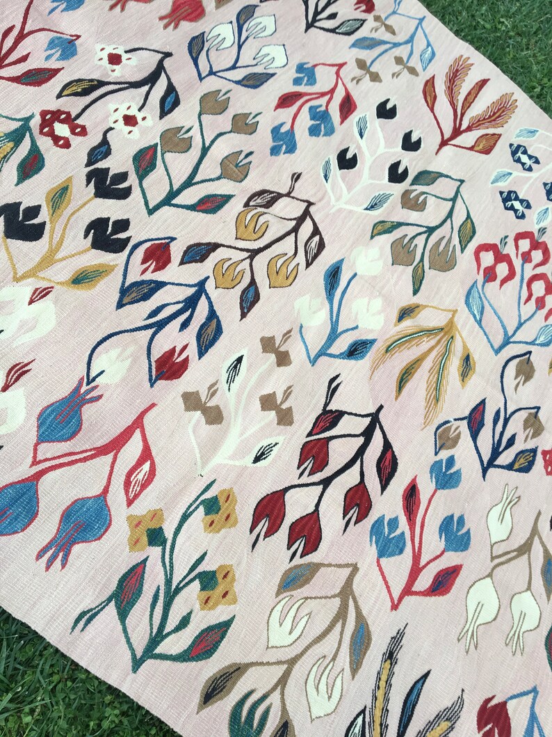 Puede incluir: Una alfombra rosa con un patr&oacute;n floral. La alfombra presenta una variedad de colores, incluyendo rojo, azul, verde y amarillo. Las flores son estilizadas y tienen un toque caprichoso.