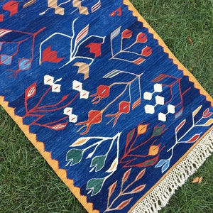May include: A blue and yellow patterned rug with a fringe border. The rug features a stylized floral design with red, white, and green accents.