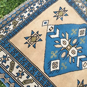 May include: A beige rug with a blue and white geometric pattern. The rug has a fringe border and features a central design with a starburst motif.