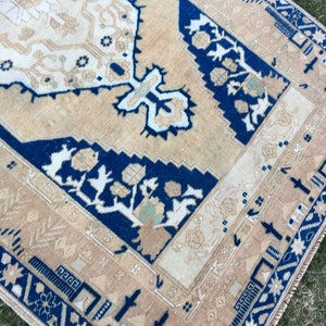May include: A beige and blue rug with a traditional floral pattern. The rug has a fringed edge and is made of wool.