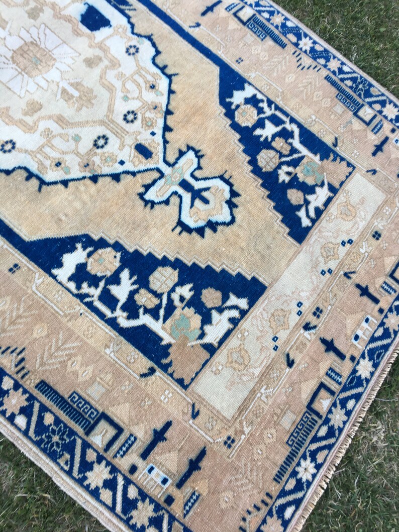 May include: A beige and blue rug with a traditional floral pattern. The rug has a fringed edge and is made of wool.