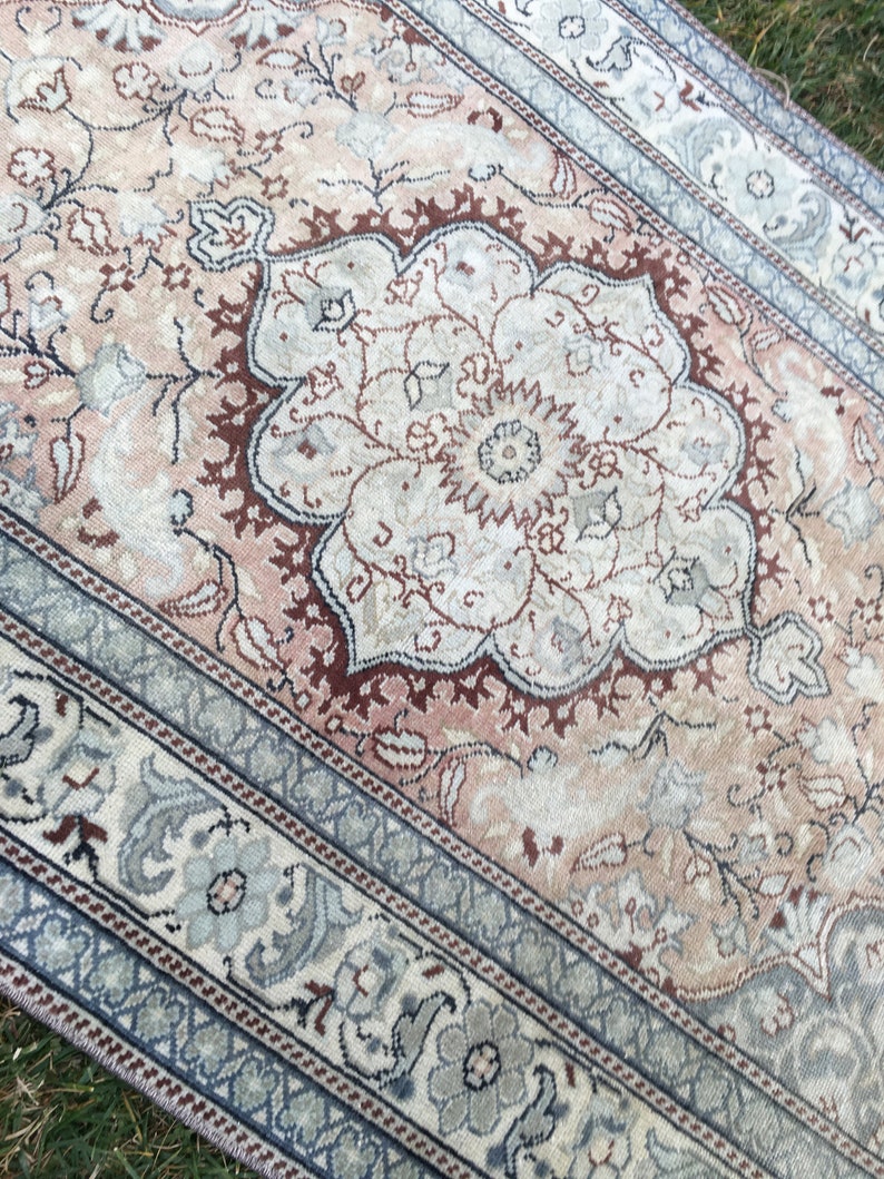 Peut inclure: Un tapis vintage avec un motif floral dans des tons de rose, marron et bleu. Le tapis a un aspect d&eacute;lav&eacute; et est fait d'un mat&eacute;riau doux et tiss&eacute;.