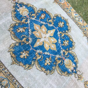 May include: A rectangular, vintage-style rug with a central medallion design. The rug features a light beige background with a large, ornate blue and gold floral pattern. The border is a darker gold with intricate detailing.