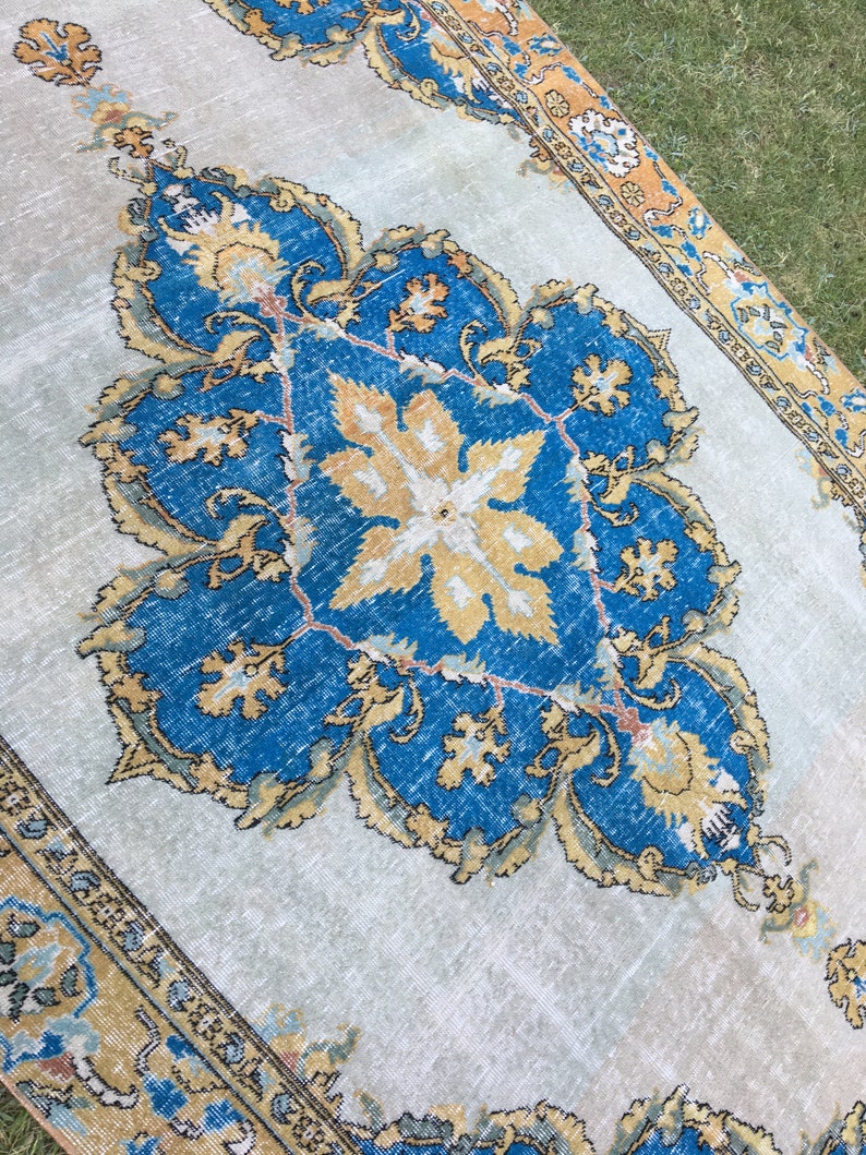 May include: A rectangular, vintage-style rug with a central medallion design. The rug features a light beige background with a large, ornate blue and gold floral pattern. The border is a darker gold with intricate detailing.