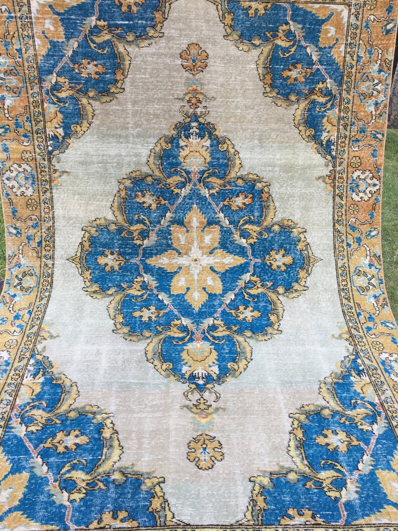 May include: A rectangular, vintage-style rug with a central medallion design. The rug features a light gray background with ornate blue and gold floral patterns. The border is a darker gold color, adding contrast.
