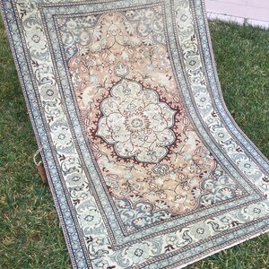 Peut inclure: Un tapis vintage avec un motif floral dans des tons beige, marron et bleu. Le tapis a un m&eacute;daillon central avec un motif floral et une bordure avec un motif r&eacute;p&eacute;titif.