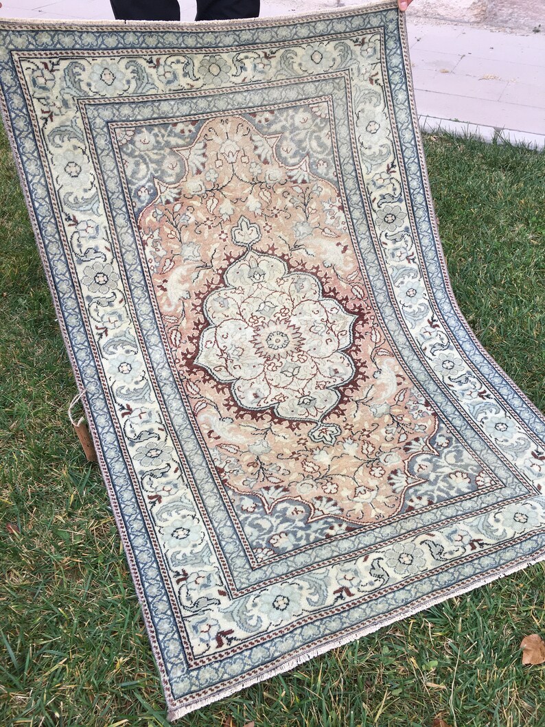 Peut inclure: Un tapis vintage avec un motif floral dans des tons beige, marron et bleu. Le tapis a un m&eacute;daillon central avec un motif floral et une bordure avec un motif r&eacute;p&eacute;titif.