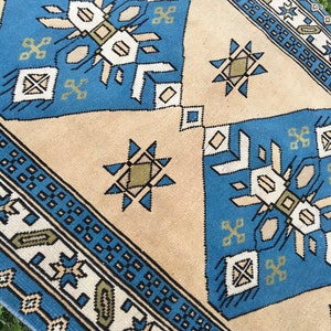 May include: A blue and beige patterned rug with geometric designs. The rug has a border with a repeating pattern of small squares.