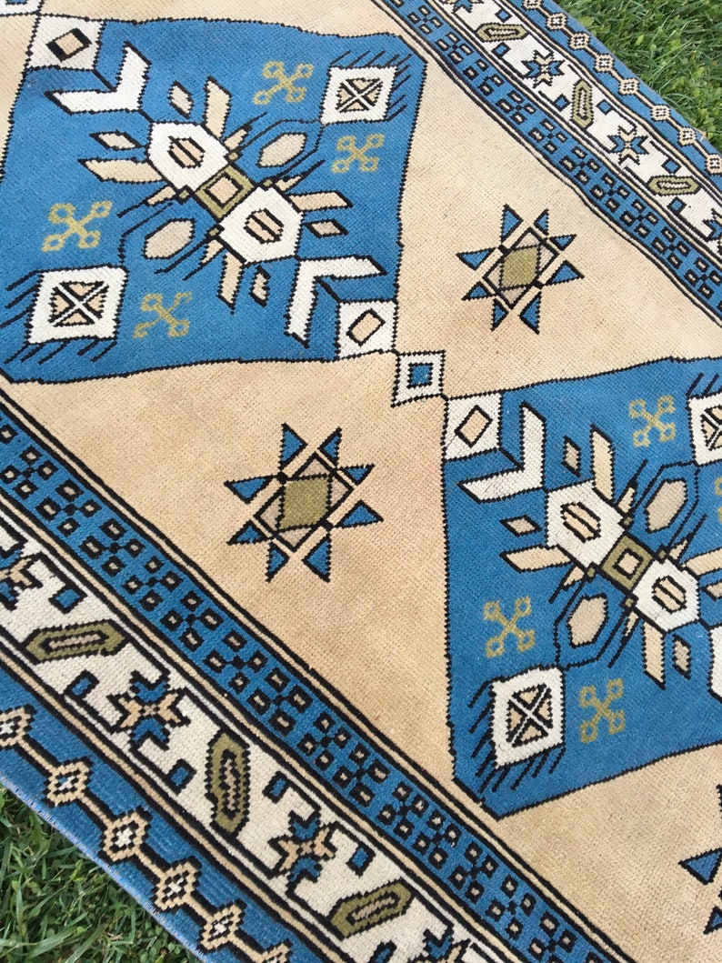 May include: A blue and beige patterned rug with geometric designs. The rug has a border with a repeating pattern of small squares.