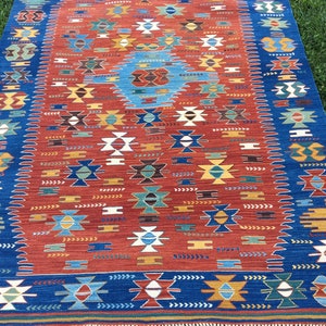 Puede incluir: Una alfombra colorida con un patr&oacute;n geom&eacute;trico en tonos rojos, azules, verdes y blancos. La alfombra tiene un borde de flecos.
