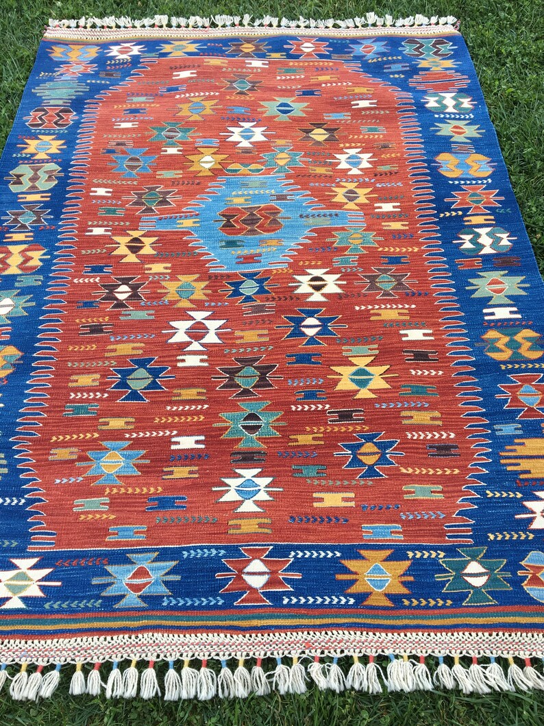 Puede incluir: Una alfombra colorida con un patr&oacute;n geom&eacute;trico en tonos rojos, azules, verdes y blancos. La alfombra tiene un borde de flecos.