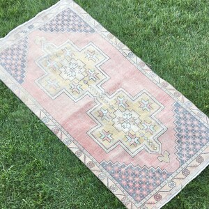 May include: A rectangular, vintage-style rug with a central geometric design in shades of pink, yellow, and beige. The rug features intricate border patterns in blue, gray, and cream, with a distressed appearance.