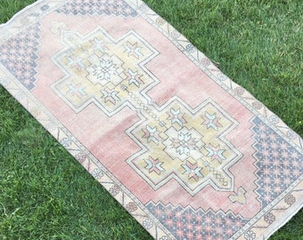 May include: A rectangular, vintage-style rug with a central geometric design in shades of pink, yellow, and beige. The rug features intricate border patterns in blue, gray, and cream, with a distressed appearance.