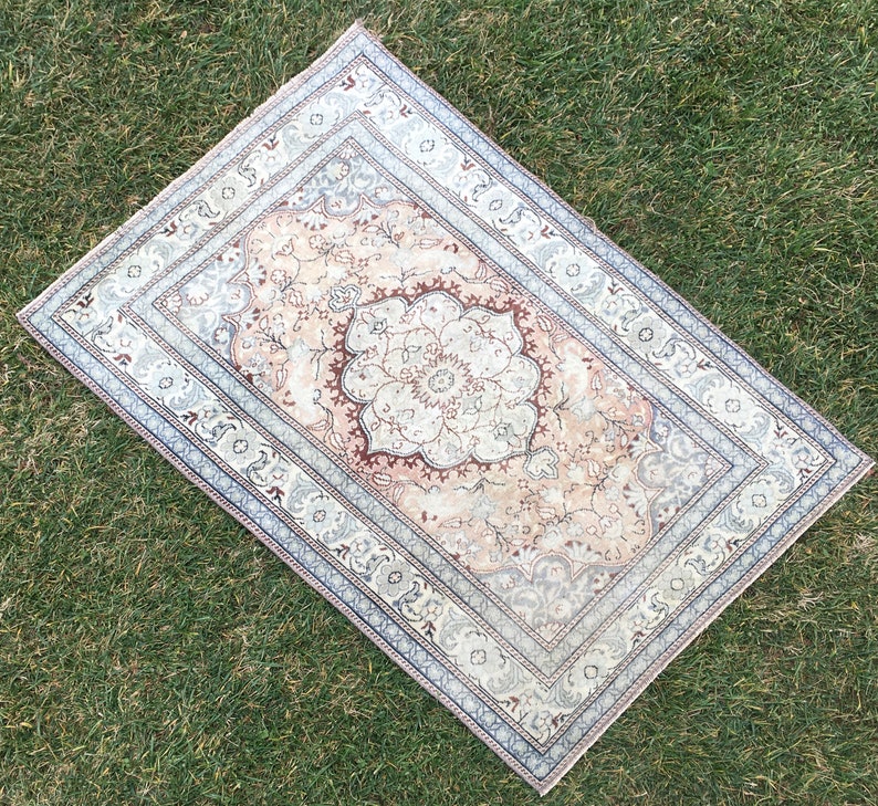 Peut inclure: Un tapis vintage avec un motif floral dans des tons beige, marron et bleu. Le tapis a un m&eacute;daillon central avec un motif floral et une bordure avec un motif r&eacute;p&eacute;titif.