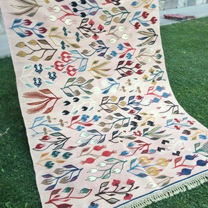 Puede incluir: Una alfombra rosa con un patr&oacute;n floral en tonos de rojo, azul, verde y amarillo. La alfombra tiene un borde de flecos.
