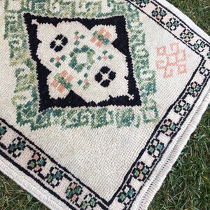 May include: A white rug with a black, green and pink geometric pattern. The rug has a fringed border.