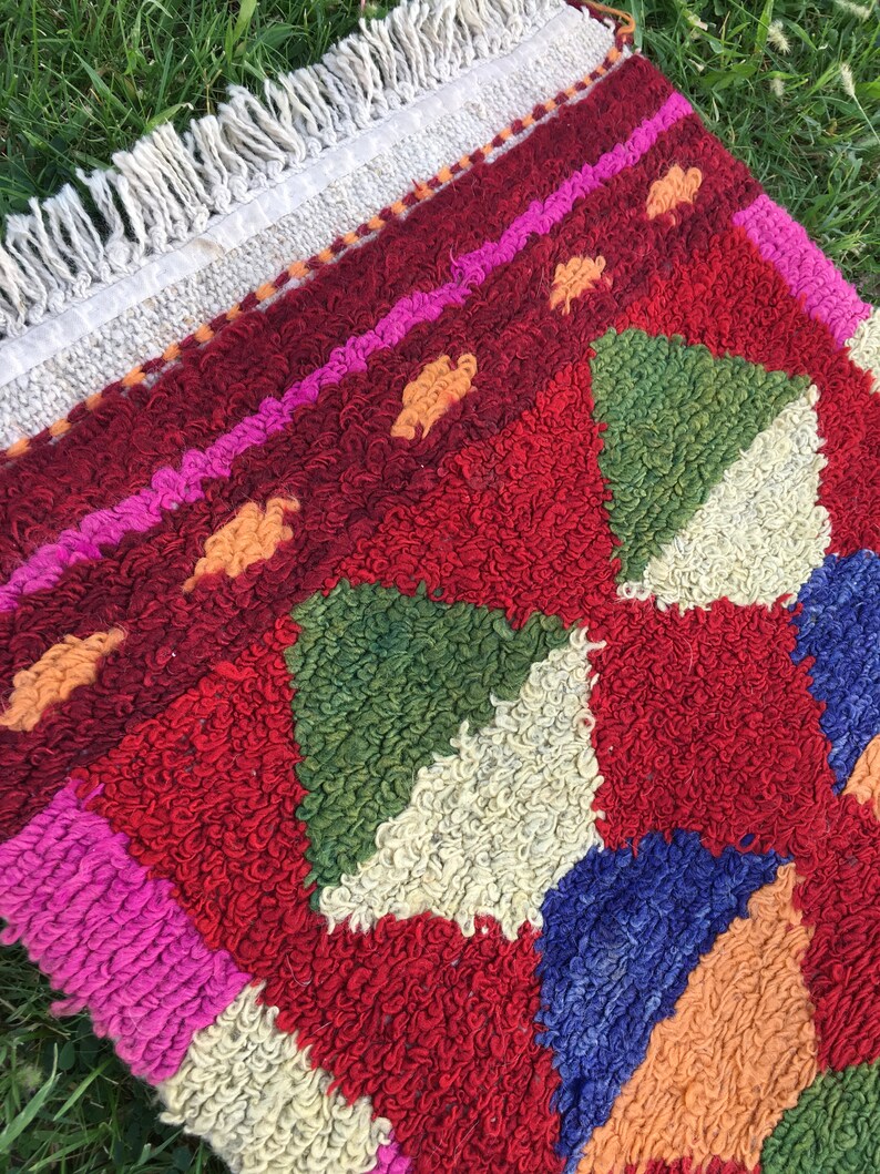 Puede incluir: Una alfombra colorida tejida a mano con un patr&oacute;n geom&eacute;trico en tonos de rojo, rosa, verde, azul y naranja. La alfombra tiene un borde de flecos.