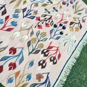 Puede incluir: Una alfombra rosa con un patr&oacute;n floral en tonos de azul, rojo, marr&oacute;n y dorado. La alfombra tiene un borde de flecos.