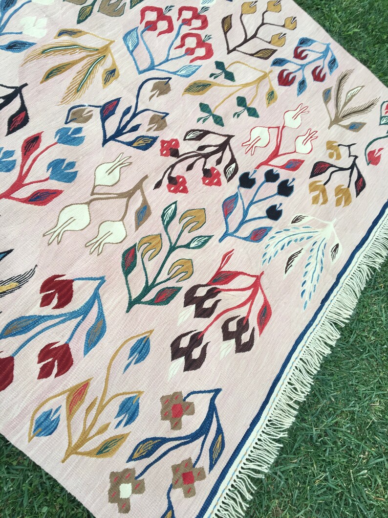 Puede incluir: Una alfombra rosa con un patr&oacute;n floral en tonos de azul, rojo, marr&oacute;n y dorado. La alfombra tiene un borde de flecos.