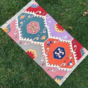May include: A colorful rug with a geometric pattern in shades of red, blue, purple, and gray. The rug has a white fringe border.