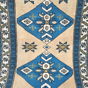May include: A beige rug with a blue and white geometric pattern. The rug has a border with a repeating pattern of blue and white squares.