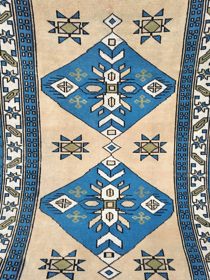 May include: A beige rug with a blue and white geometric pattern. The rug has a border with a repeating pattern of blue and white squares.