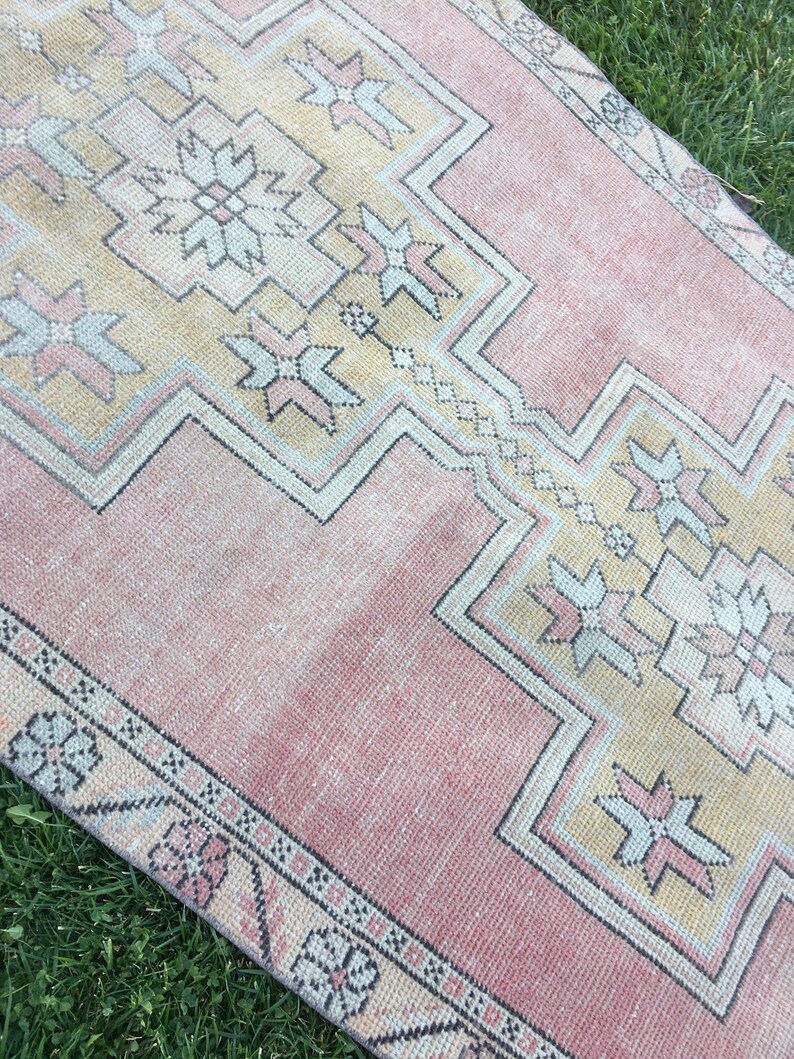 May include: A rectangular, vintage-style rug with a faded, distressed appearance. The rug features a central design in shades of peach and beige, with geometric patterns and floral motifs. The border is a darker peach color with repeating floral elements.