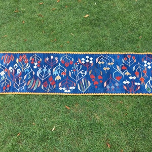 May include: A blue and yellow runner rug with a floral pattern. The rug has a fringe on both ends.