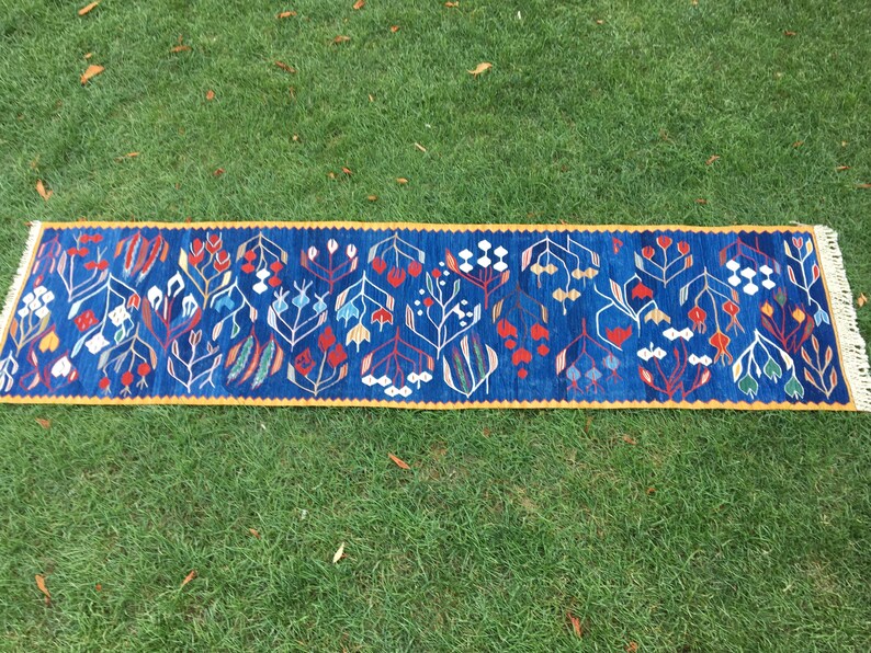 May include: A blue and yellow runner rug with a floral pattern. The rug has a fringe on both ends.