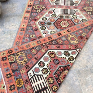 May include: A traditional Turkish rug with a colorful geometric pattern. The rug is folded in half, revealing a cream-colored background with intricate designs in shades of red, blue, green, and yellow.