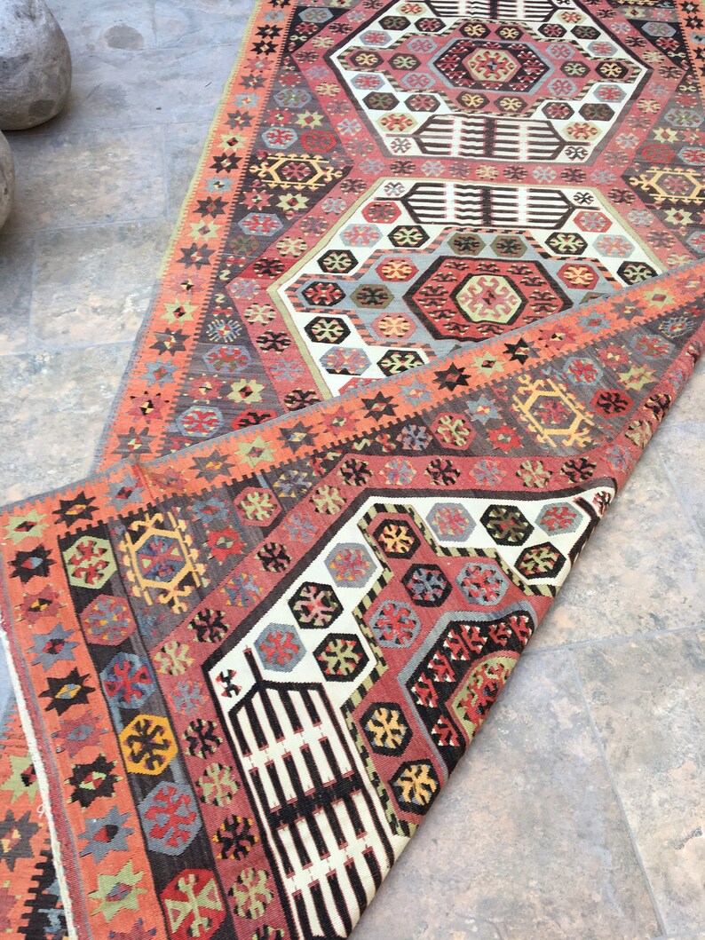 May include: A traditional Turkish rug with a colorful geometric pattern. The rug is folded in half, revealing a cream-colored background with intricate designs in shades of red, blue, green, and yellow.