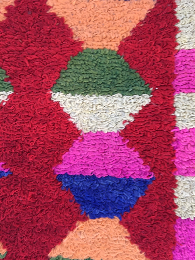 Puede incluir: Primer plano de una alfombra colorida y texturizada con formas geom&eacute;tricas en tonos rojos, verdes, blancos, rosas, azules y naranjas.