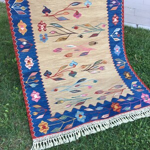 May include: A beige rug with a blue border and a floral pattern. The rug has a fringe on all sides.