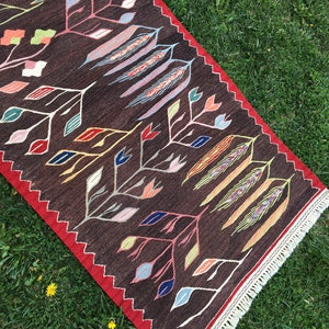 Puede incluir: Una alfombra marr&oacute;n con un estampado floral colorido. La alfombra tiene un borde rojo y flecos blancos.