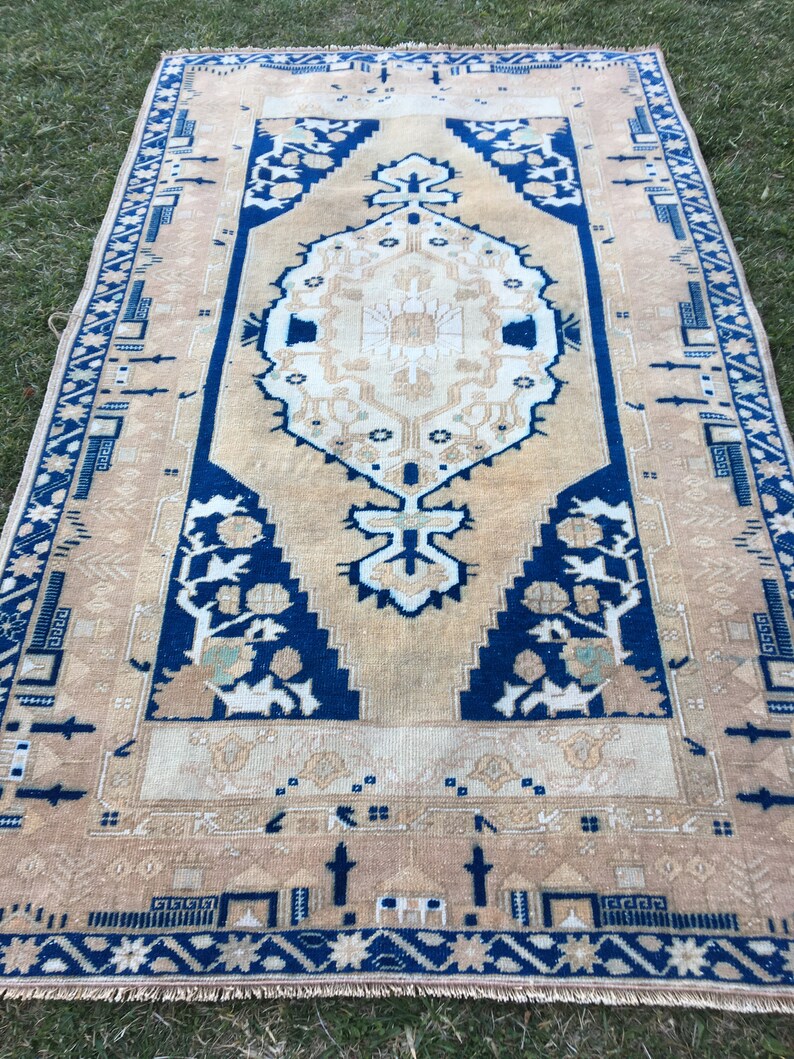 May include: A vintage rug with a beige background and a blue and white geometric pattern. The rug has a fringe border.