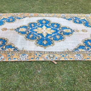 May include: A rectangular rug with a central medallion design. The rug features a light beige background with a large, ornate blue and yellow floral pattern. The border is a mix of yellow and blue, creating a vintage aesthetic.