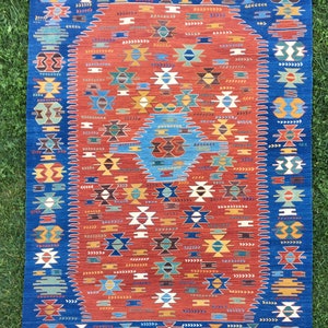 Puede incluir: Una alfombra turca tradicional con un esquema de color azul y rojo. La alfombra presenta un medall&oacute;n oval central con intrincados patrones geom&eacute;tricos. La alfombra tiene un borde de flecos.
