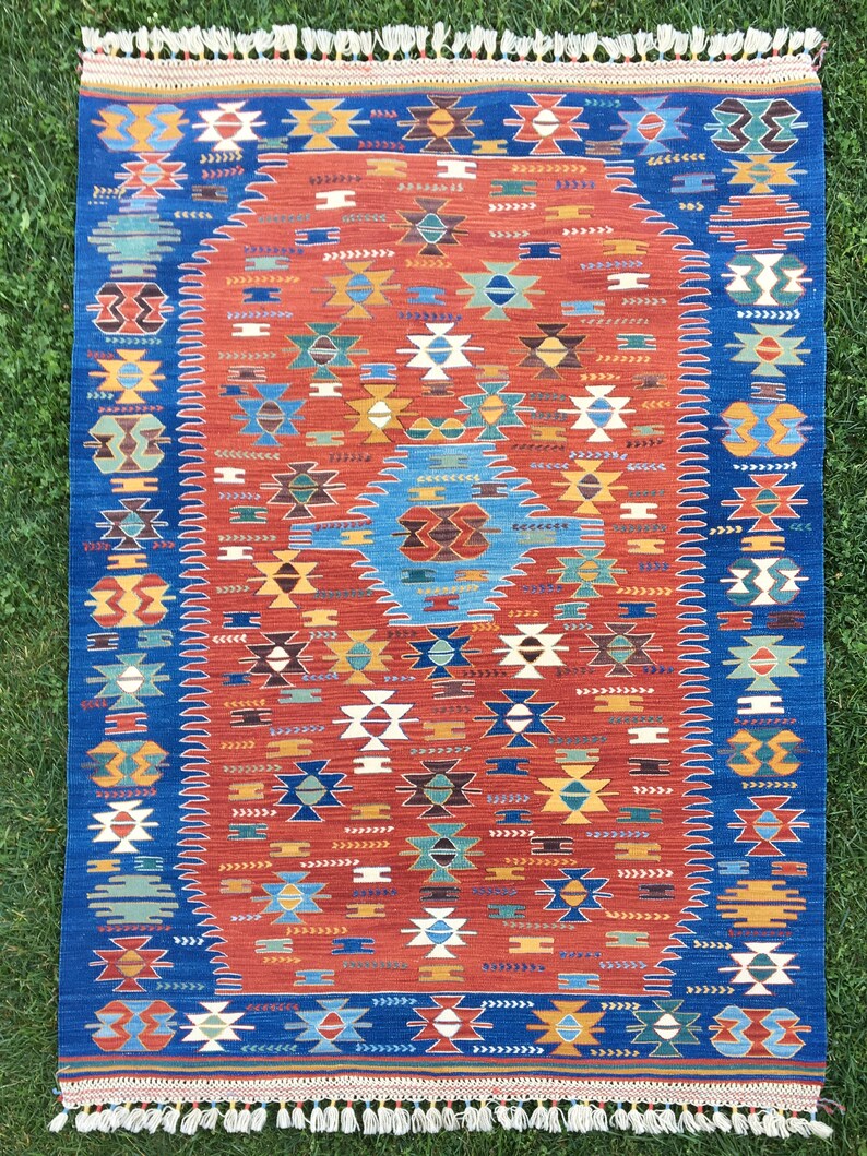 Puede incluir: Una alfombra turca tradicional con un esquema de color azul y rojo. La alfombra presenta un medall&oacute;n oval central con intrincados patrones geom&eacute;tricos. La alfombra tiene un borde de flecos.