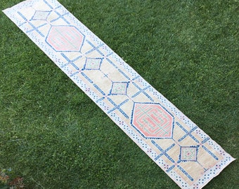 May include: A beige runner rug with a geometric pattern in shades of pink, blue, and green. The rug has a traditional design with repeating diamond shapes and cross patterns.
