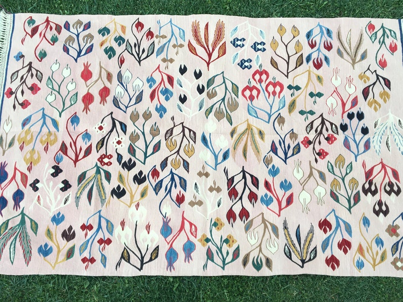 Puede incluir: Una alfombra rosa con un patr&oacute;n floral. La alfombra presenta una variedad de colores, incluyendo rojo, azul, verde, amarillo y blanco. Las flores son estilizadas y abstractas, y la alfombra tiene un aspecto tejido a mano.