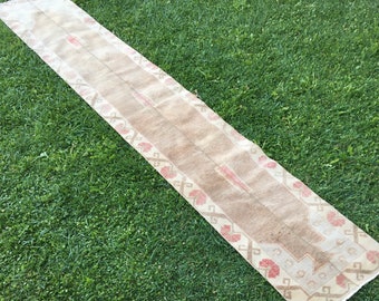 May include: A long, off-white runner rug with a brown and pink geometric pattern. The rug is laid out on a green grassy lawn.