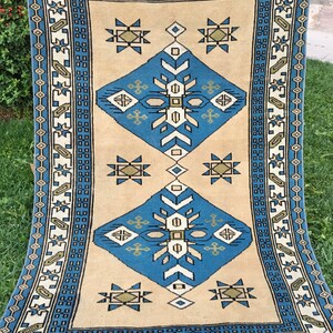May include: A vintage rug with a geometric pattern in shades of blue, green, and beige. The rug has a fringe border and is woven with a traditional design.