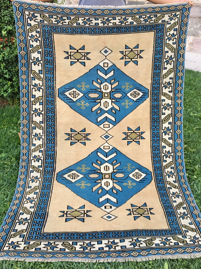 May include: A vintage rug with a geometric pattern in shades of blue, green, and beige. The rug has a fringe border and is woven with a traditional design.